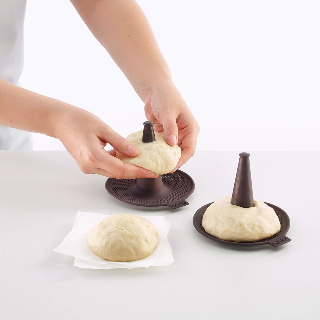 Person shaping dough with a cone-shaped tool on a white background