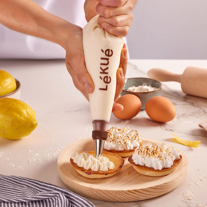 Person using a Lékué piping bag to fill small pastries with cream on a kitchen counter.