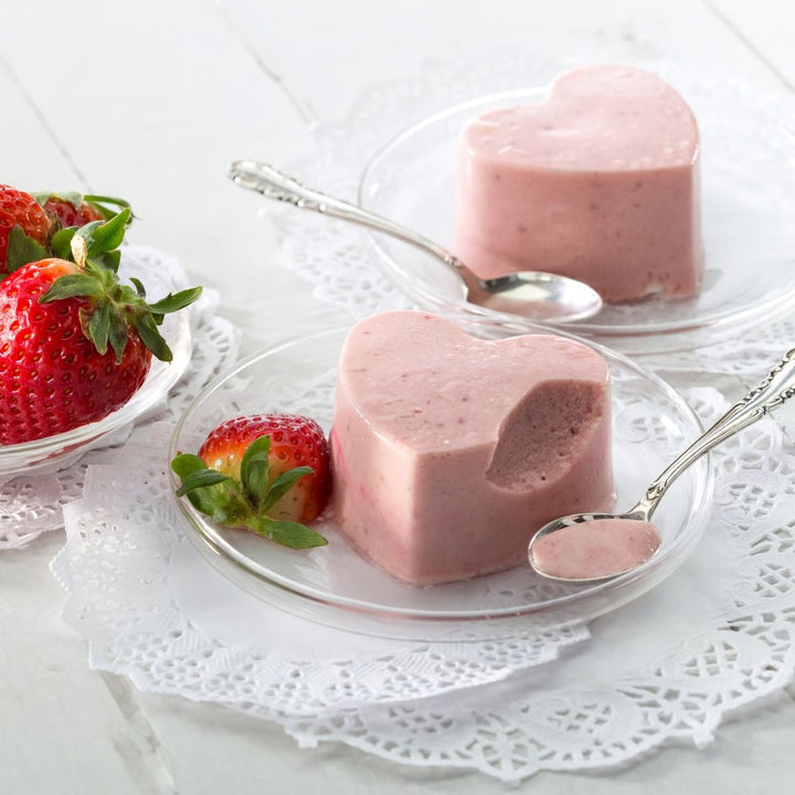 Heart-shaped strawberry desserts on clear plates with fresh strawberries on a white lace tablecloth.